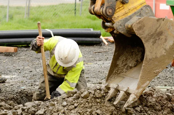 Lucrător în construcții lângă utilaj pe șantier